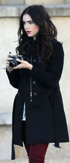 a woman in black coat and red pants holding a camera