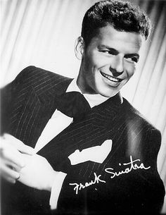 a black and white photo of a man in a suit with his arms crossed, smiling