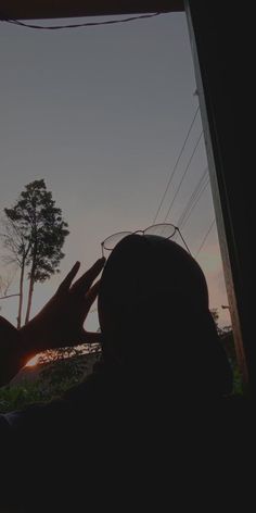 the silhouette of a person holding their hands up in front of an open window at sunset