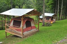 two tents are set up in the woods with picnic tables and benches around them for people to sit on