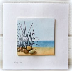 a painting of rocks and sea grass on a white card with the ocean in the background