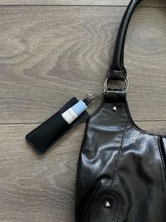 a black purse with a tag attached to it sitting on a wooden floor next to a wallet