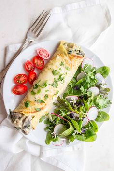 a white plate topped with an omelet next to a green salad and fork