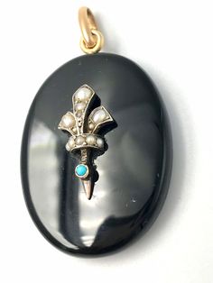 This large and beautiful antique pendant was crafted in Victorian Era as a mourning pendant to remember a loved one.  - Obverse: created from black onyx, it has a detailed arrangement of a pearl fleur de lis set in silver in the center of the front of the pendant. -Reverse: The piece has glass framed in an 18k gold frame. Inside is a photograph of a young Victorian woman, which can be removed. The hook is also 18k gold. Excellent condition. Circa 1880. Attention: light or shadow that may appear Historical Yellow Gold Jewelry For Wedding, Historical Yellow Gold Wedding Jewelry, Black Heirloom Jewelry For Ceremonial Occasions, Black Heirloom Jewelry For Ceremonial Use, Black Heirloom Ceremonial Jewelry, Victorian Cabochon Oval Pendant Jewelry, Black Cabochon Victorian Jewelry, Victorian Black Cabochon Jewelry, Victorian Cabochon Ceremonial Jewelry