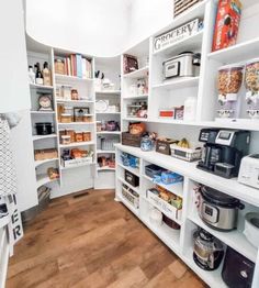 a kitchen with lots of white shelves filled with food and cooking supplies on top of wooden floors