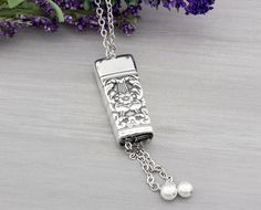 a necklace with a lighter and pearls hanging from it's side on a table next to purple flowers