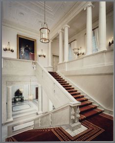 a staircase leading up to the first floor in a large room with columns and chandelier