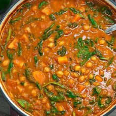 a large pot filled with lots of food on top of a wooden table next to a spoon