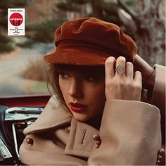 a woman wearing a brown hat and trench coat holding her hand up to her head