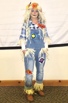 a woman dressed up as a scarecrow with flowers on her head and blue overalls