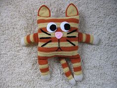 a crocheted orange and white cat laying on top of a floor next to a rug