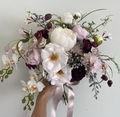 a bouquet of flowers is being held by someone's hand in front of a white wall