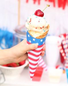 a person holding an ice cream cone with a cherry on top and sprinkles