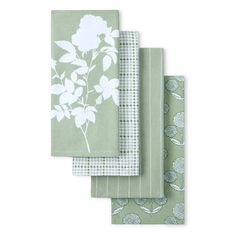 four green napkins with white flowers and leaves on them, each folded in different patterns