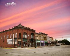 an old brick building sitting on the side of a road next to tall buildings at sunset