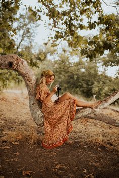 a woman sitting on a tree branch holding a camera