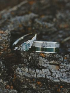 two wedding rings sitting on top of a piece of wood next to another ring with an aqua blue stone