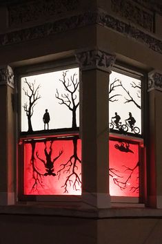 the silhouettes of two people on bicycles are seen through an illuminated window