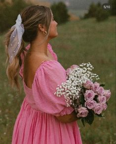 a woman in a pink dress holds a bouquet of flowers and looks up into the sky