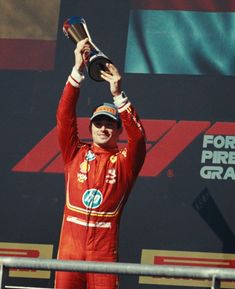 a man holding up a trophy on top of a race track with his hands in the air