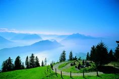 people are sitting on the top of a grassy hill with mountains in the back ground