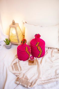 two pink baskets sitting on top of a bed next to a lamp and potted plant