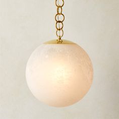 a white ball hanging from a gold chain on a light fixture with a beige background