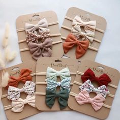 four small bows are on top of each other in different colors and sizes, sitting next to some dried grass