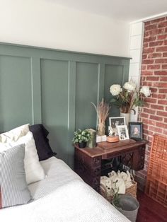 a bedroom with brick wall and green painted headboard, white bedding and pillows