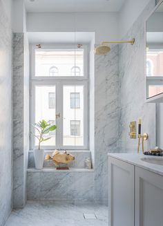 a bathroom with white marble walls and flooring next to a bathtub in front of a window