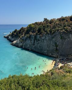 people are swimming in the clear blue water near an island with cliffs and trees on either side