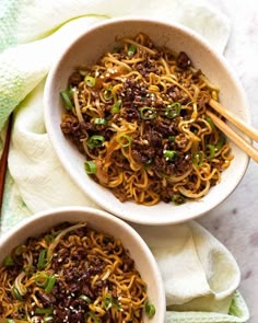 two bowls filled with noodles and meat on top of a white cloth next to chopsticks