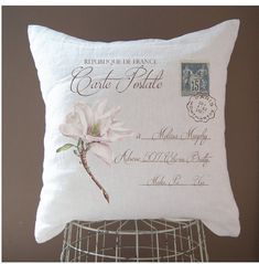 a white pillow with a pink flower on it and a postage stamp in the back