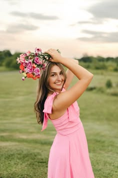 a beautiful young woman in a pink dress holding a bouquet of flowers over her head