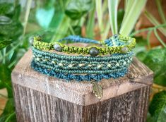 three different bracelets sitting on top of a wooden post in front of green plants