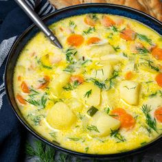 a bowl of soup with carrots, potatoes and dill in it next to some bread