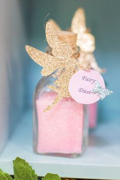 a bottle filled with pink and gold glitter sitting on top of a shelf