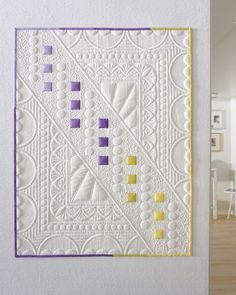 a white wall with a purple and yellow quilt on it