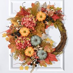 a wreath with leaves, berries and acorns hanging on a white door frame