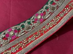 an embroidered red and green cloth with gold trimmings on the edge, sitting on a pink surface