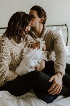 a man and woman kissing while holding a baby in their arms on a bed with white sheets