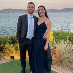 a man and woman standing next to each other in front of a body of water