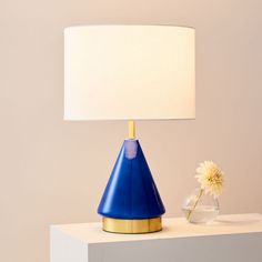 a blue lamp sitting on top of a table next to a vase with a flower