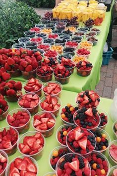 many bowls of strawberries and oranges are on the table with people standing behind them