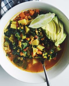 a white bowl filled with soup and topped with an avocado slice on top