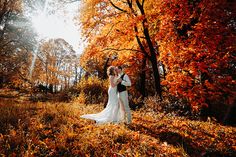 a bride and groom standing in the middle of an autumn forest holding each other's hands