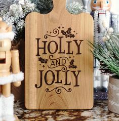 a wooden cutting board with the words holly and jolly on it next to christmas decorations