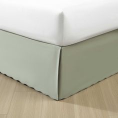 a bed with a white and green bedspread on it's side next to a wooden floor