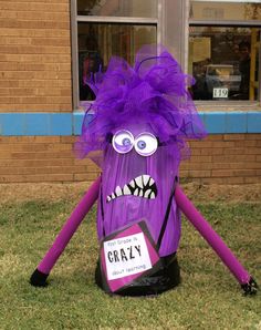 a purple monster sitting on top of a grass covered field in front of a building