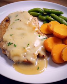 a white plate topped with meat covered in gravy next to green beans and carrots